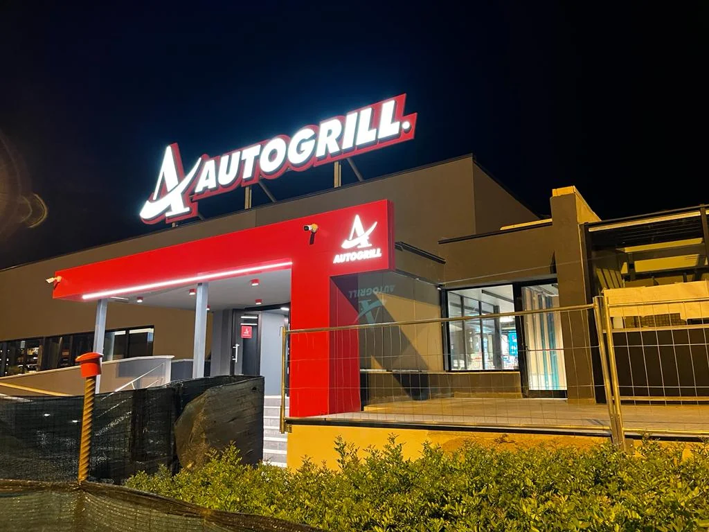 Portale rosso in Alucobond con insegna Autogrill a Badia al Pino, fotografato di notte.
