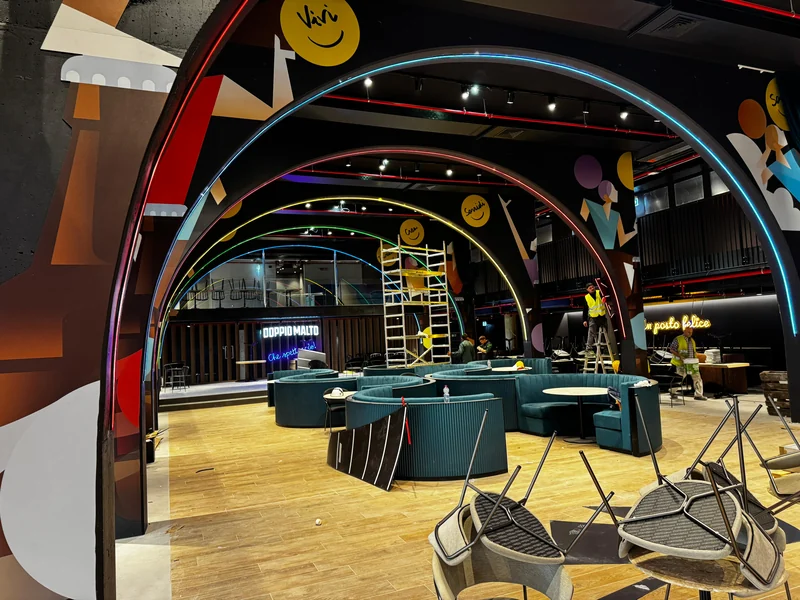 Archi con profili luminosi e grafiche negli spazi Chorus Life, con squadre e attrezzature di cantiere.
