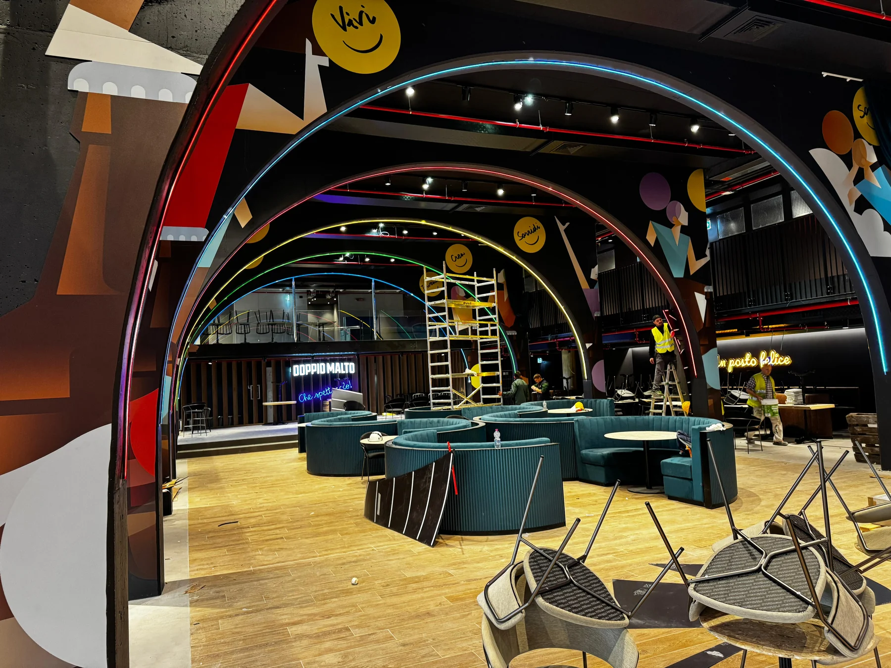 Archi con profili luminosi e grafiche negli spazi Chorus Life, con squadre e attrezzature di cantiere.