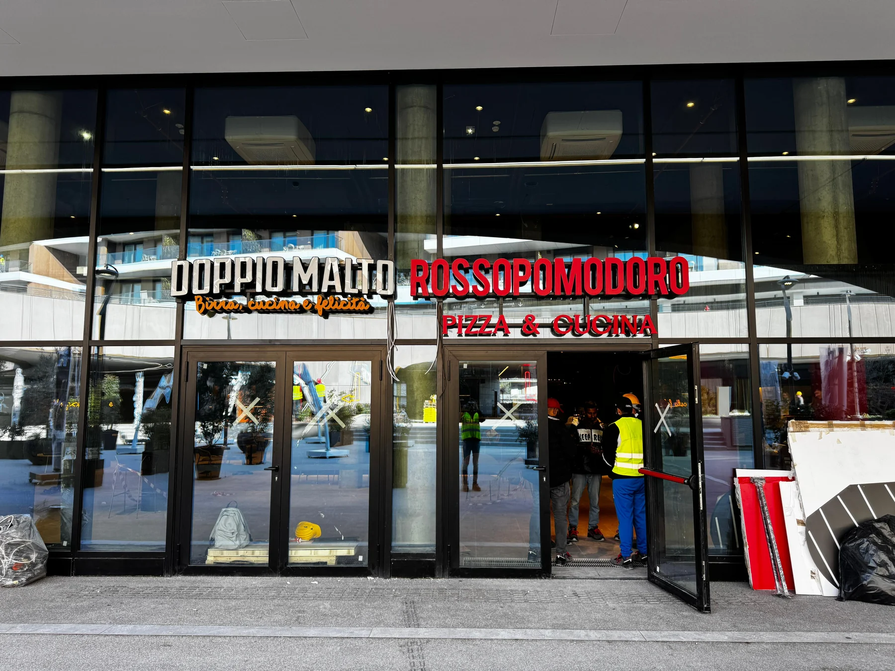 Insegne Doppio Malto e Rossopomodoro sulla vetrata di ingresso, con lavori in corso.