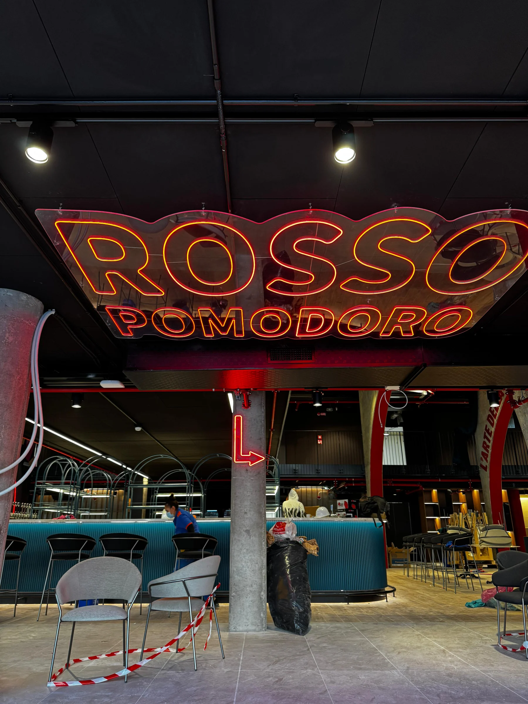 Scritta luminosa Rossopomodoro sospesa negli interni, con materiali e attrezzature ancora presenti.
