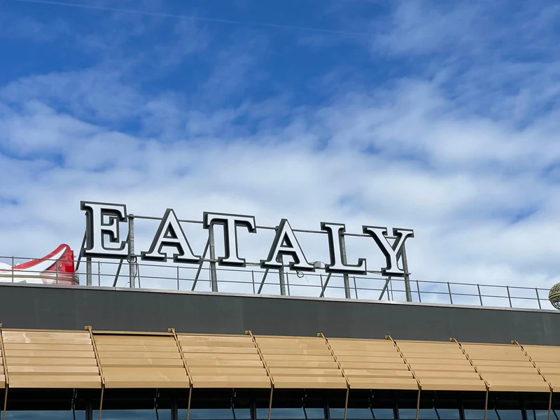 Insegna Eataly sopra la facciata del punto di ristoro autostradale di Dorno, sotto un cielo azzurro.