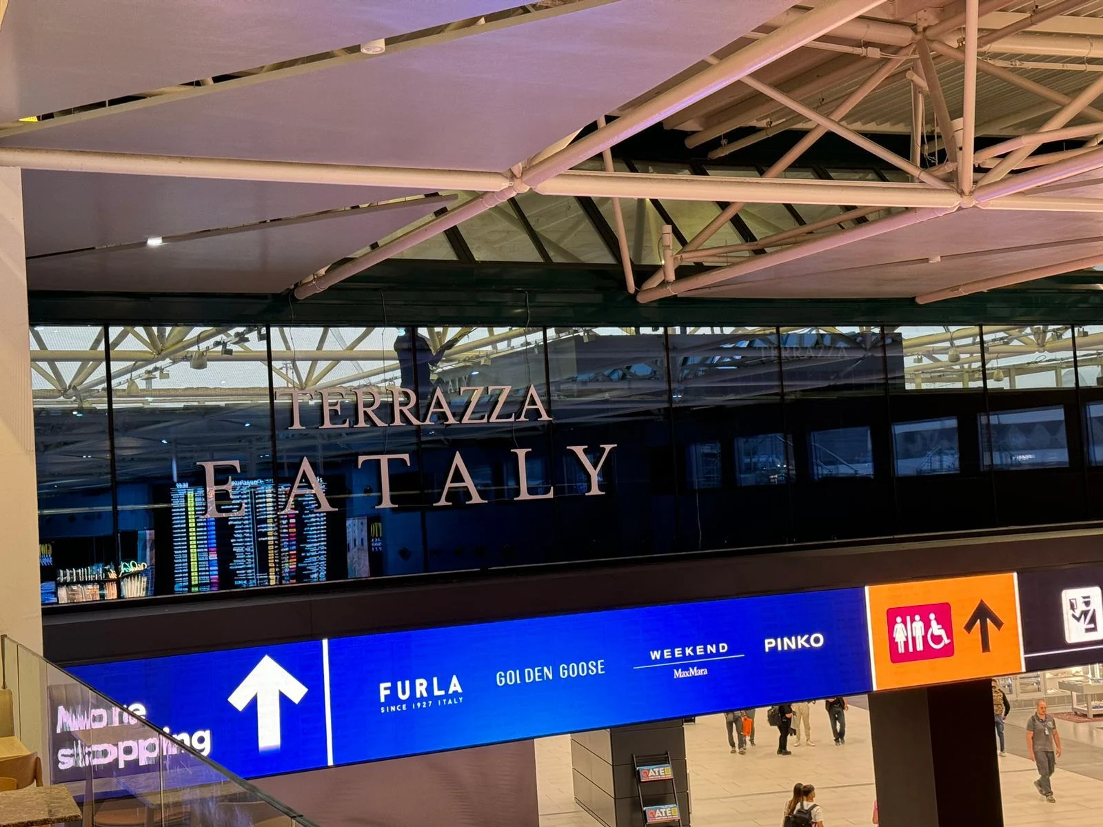 Dettaglio dell’insegna Terrazza Eataly sulla vetrata, con i riflessi dell’ambiente aeroportuale.